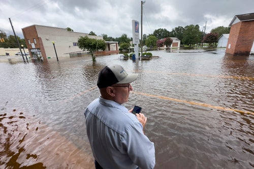 Randy Sikes speaks to his relatives on a mobile phone as he stands in residual rain water flooding the downtown area caused by Tropical Storm Debby, on Aug. 8, 2024, in Bladenboro, NC.