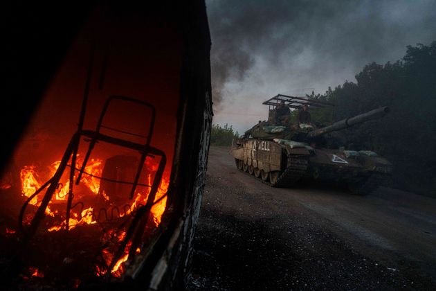 A Ukrainian tank passes by a burning car near the Russian-Ukrainian border, Sumy region, Ukraine, Wednesday, August 14.