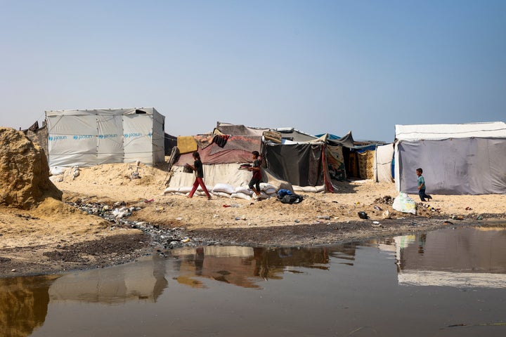 Children walk next to garbage and raw sewage at a camp for displaced Palestinians in Deir al-Balah in the central Gaza Strip on Aug. 19.