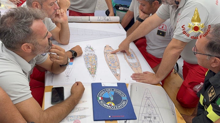 Scuba divers study a map of the sailing yacht Bayesian at the Porticello harbor on Tuesday amid search and rescue efforts. 