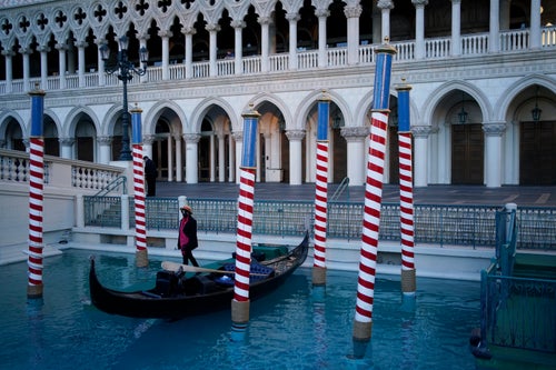 A gondolier stands by a boat near a quiet pedestrian walkway at the Venetian hotel and casino in Las Vegas, Feb. 4, 2021. (AP Photo/John Locher)