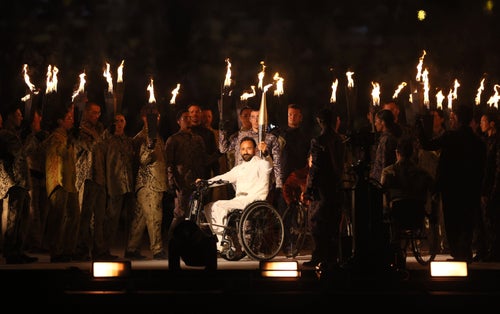 Performers hold flames as a torchbearer carries the Paralympic Flame.