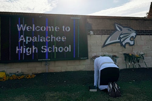 A person kneels in front of flowers that are placed outside the entrance to Apalachee High School in Winder, Georgia, on Thursday, Sept. 5.