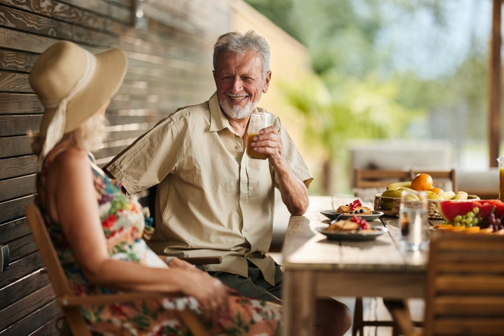 Happy mature man drinking juice while communicating with his wife on a patio.