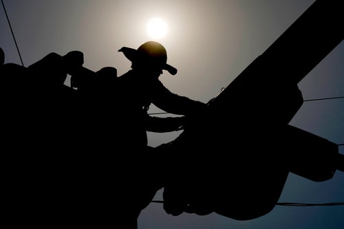 A linesman works on power lines under the morning sun, July 12, 2024, in Phoenix.