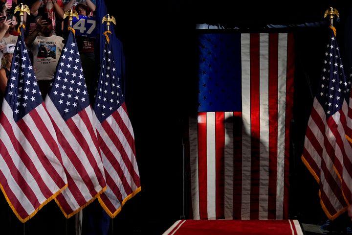 The silhouette of Republican presidential nominee former President Donald Trump is seen as he pauses behind an American Flag as he arrives to speak at a campaign rally at the Mohegan Arena at Casey Plaza, Saturday, Aug. 17. 2024, in Wilkes-Barre, Pa. (AP Photo/Carolyn Kaster)