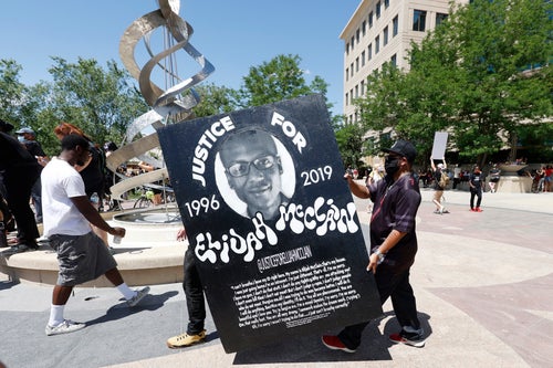 Demonstrators carry a giant placard during a rally and march over the death of 23-year-old Elijah McClain, Saturday, June 27, 2020, outside the police department in Aurora, Colorado.