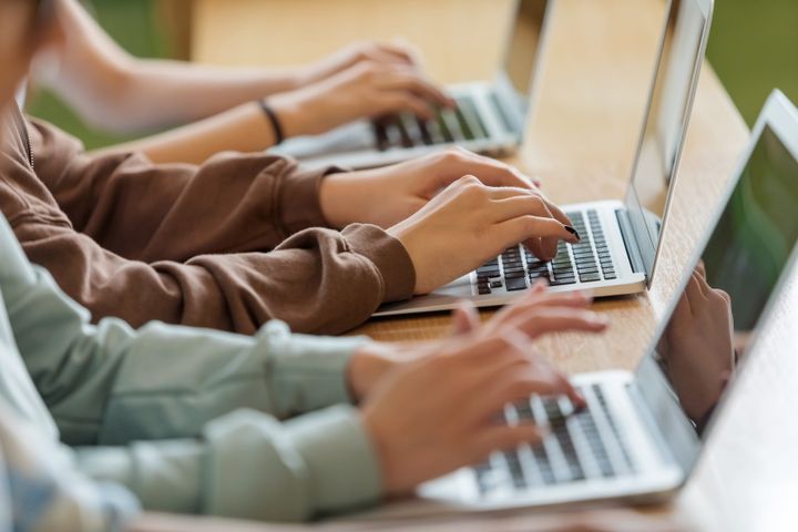 High school students sitting at the desk in the classroom during lesson, using laptops. Close up of hands, unrecognizable people.