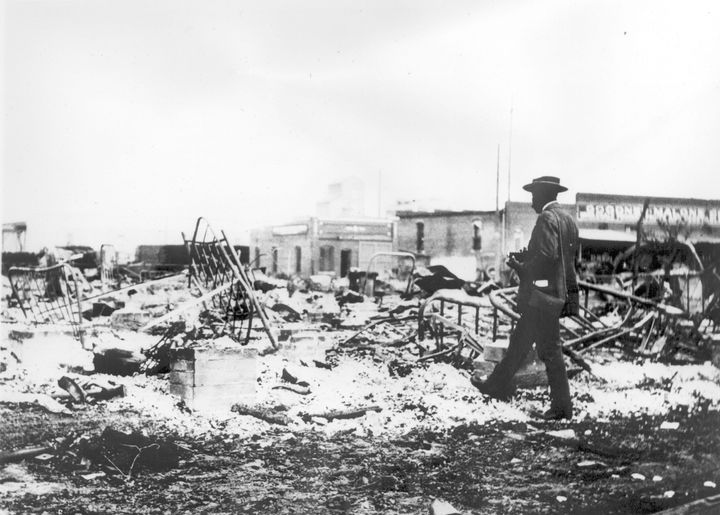 Ein Mann untersucht die Skelette von Eisenbetten, die sich über der Asche einer verbrannten Masse nach dem Massaker von Tulsa Race erheben.