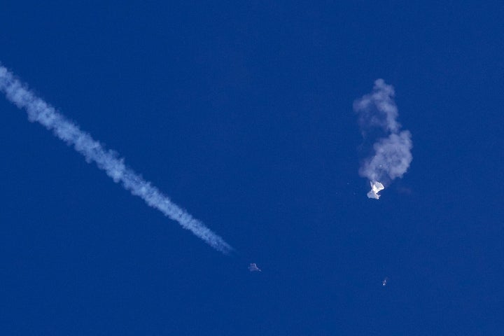 A fighter jet flies near the remnants of a large balloon after it was struck by a missile off the coast of South Carolina near Myrtle Beach on Feb. 4, 2023.