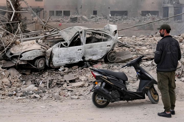 A man stands in front of a destroyed car at a scene hit by Israeli airstrikes in Dahiyeh, Beirut, Lebanon, Monday, Oct. 7, 2024. (AP Photo/Hussein Malla)