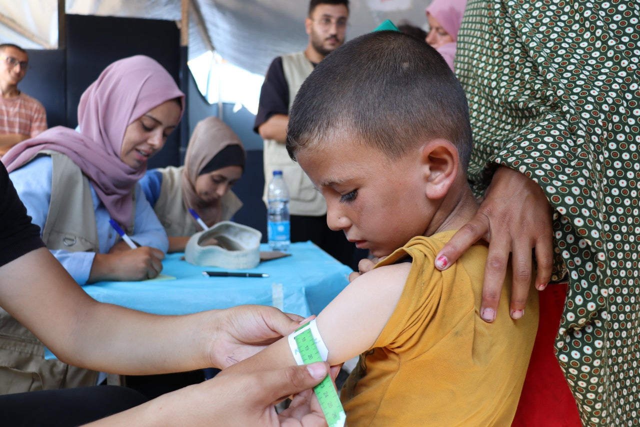 An aid worker measures the upper arm of a Palestinian child to determine the severity of malnutrition.