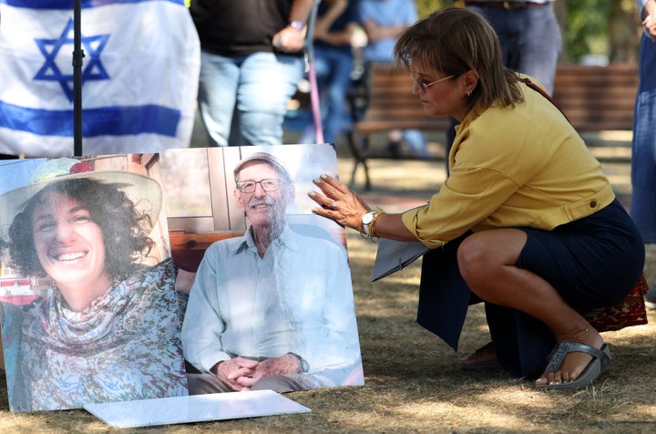 Dr. Mira Zinger, a personal family friend of Carmel Gat, knelt down to pick up photos of both Gat and 84-year-old hostage Oded Lifshitz after the wind blew them over during a rally for the hostages in Newton, Massachusetts.