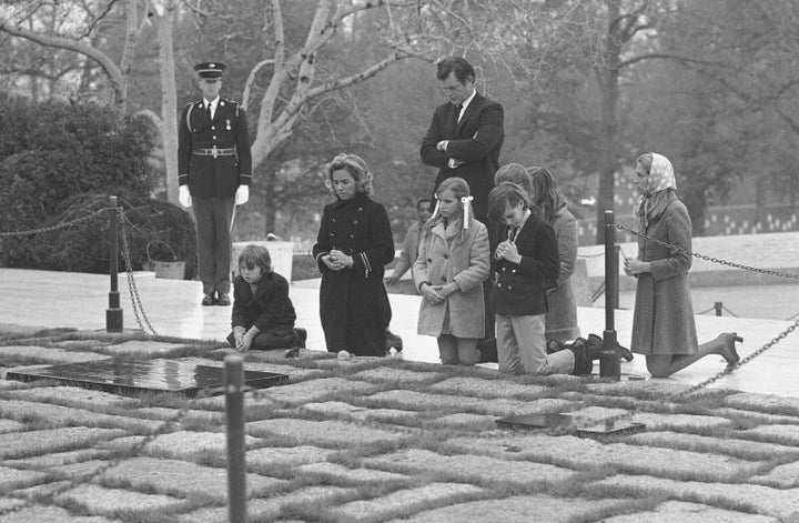 Sen. Edward Kennedy, back, stands behind the widow of former Senator Robert F. Kennedy, Mrs. Ethel Kennedy, second left, with her five children, and his wife Joan, right, as they pause at the grave of assassinated President John F. Kennedy in Arlington National Cemetery, Nov. 20, 1970, in Arlington, Va. (AP Photo/Bob Daugherty, File)