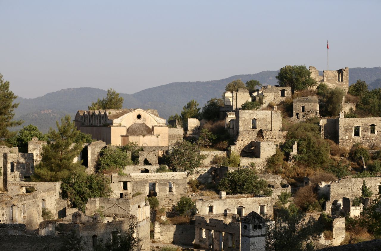 MUGLA, ΤΟΥΡΚΙΑ - 25 ΙΟΥΝΙΟΥ: Άποψη του Kayakoy, το οποίο είναι επίσης γνωστό ως "πόλη-φάντασμα" επειδή εγκαταλείφθηκε πριν από χρόνια και συγκαταλέγεται στις ευαίσθητες περιοχές που πρέπει να προστατευθούν αυστηρά στην περιοχή Fethiye της Mugla, στην Τουρκία, στις 25 Ιουνίου 2024. Το Kayakoy, ή Levissi στα ελληνικά, είναι ένα χωριό στο Fethiye της νοτιοδυτικής Τουρκίας, όπου ζούσαν Έλληνες της Ανατολίας μέχρι περίπου το 1923. Η πόλη-φάντασμα, που σήμερα διατηρείται ως μουσειακό χωριό, αποτελείται από εκατοντάδες ετοιμόρροπα αλλά ακόμα ως επί το πλείστον άθικτα σπίτια και εκκλησίες ελληνικού τύπου, τα οποία καλύπτουν μια μικρή βουνοπλαγιά και χρησιμεύουν ως σημείο στάσης για τους τουρίστες που επισκέπτονται το Φετιγιέ και το κοντινό Ολουντενίζ. Χτίστηκε στη θέση της αρχαίας πόλης της Καρμύλης τη δεκαετία του 1700. Μετά τον ελληνοτουρκικό πόλεμο, το Καγιάκοϊ εγκαταλείφθηκε σε μεγάλο βαθμό μετά την υπογραφή συμφωνίας ανταλλαγής πληθυσμών από την τουρκική και την ελληνική κυβέρνηση το 1923. (Φωτογραφία: Ali Riza Akkir/Anadolu via Getty Images)