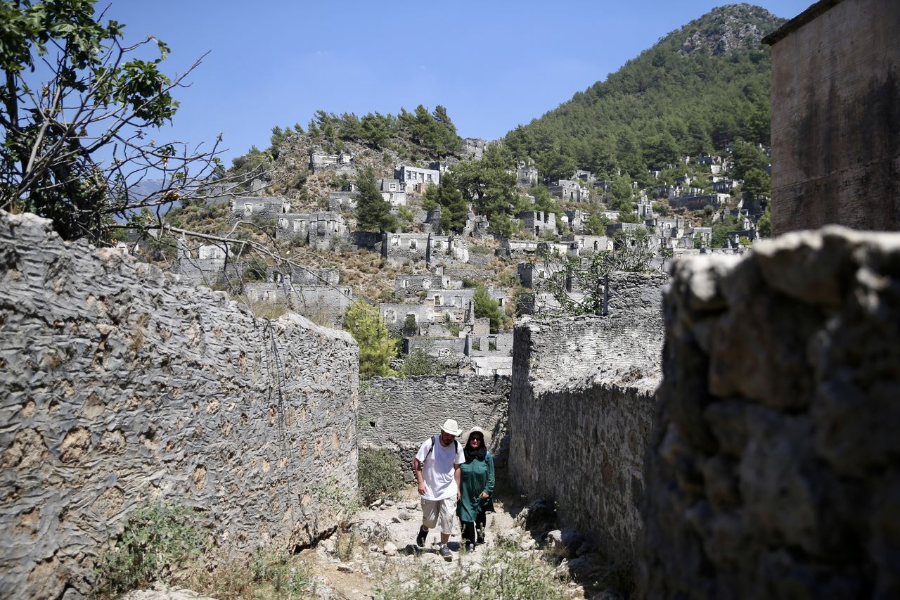 MUGLA, ΤΟΥΡΚΙΑ - 25 ΙΟΥΝΙΟΥ: Άνθρωποι επισκέπτονται το Kayakoy, το οποίο είναι επίσης γνωστό ως "πόλη-φάντασμα" επειδή εγκαταλείφθηκε πριν από χρόνια και συγκαταλέγεται στις ευαίσθητες περιοχές που πρέπει να προστατευθούν αυστηρά στην περιοχή Fethiye της Mugla, Τουρκία, στις 25 Ιουνίου 2024. Το Kayakoy, ή Levissi στα ελληνικά, είναι ένα χωριό στο Fethiye της νοτιοδυτικής Τουρκίας όπου ζούσαν Έλληνες της Ανατολίας μέχρι περίπου το 1923. Η πόλη-φάντασμα, που σήμερα διατηρείται ως μουσειακό χωριό, αποτελείται από εκατοντάδες ετοιμόρροπα αλλά ακόμα ως επί το πλείστον άθικτα σπίτια και εκκλησίες ελληνικού τύπου, τα οποία καλύπτουν μια μικρή βουνοπλαγιά και χρησιμεύουν ως σημείο στάσης για τους τουρίστες που επισκέπτονται το Φετιγιέ και το κοντινό Ολουντενίζ. Χτίστηκε στη θέση της αρχαίας πόλης της Καρμύλης τη δεκαετία του 1700. Μετά τον ελληνοτουρκικό πόλεμο, το Καγιάκοϊ εγκαταλείφθηκε σε μεγάλο βαθμό μετά την υπογραφή συμφωνίας ανταλλαγής πληθυσμών από την τουρκική και την ελληνική κυβέρνηση το 1923. (Φωτογραφία: Ali Riza Akkir/Anadolu via Getty Images)