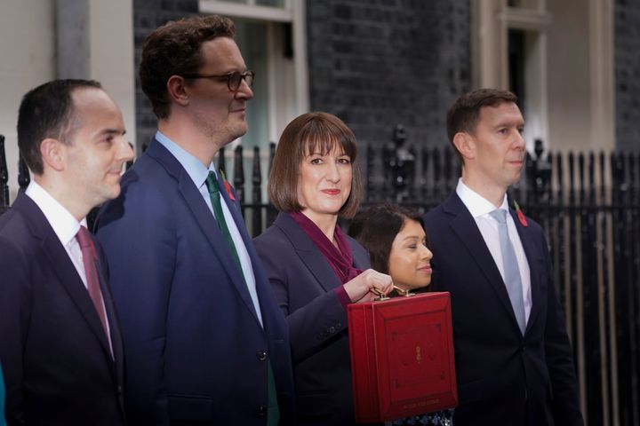 Rachel Reeves, holds up the traditional red ministerial box containing her budget speech, as she poses with her ministerial team outside 11 Downing Street.