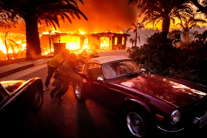 Firefighters and sheriff's deputies push a vintage car away from a burning home as the Mountain Fire burns in Camarillo, Calif., on Nov. 6, 2024.