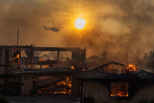 A firefighting helicopter flies near as a home burns from the Mountain Fire on Nov. 6, 2024, in Camarillo, California.
