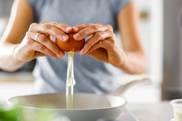 Close up of unrecognizable woman cracking an egg into a bowl.