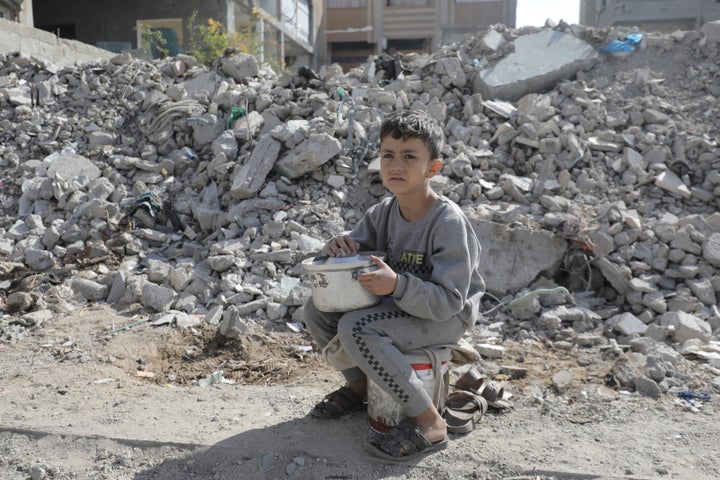 A Palestinian boy sits by rubble with a pot waiting to receive the food distributed in Gaza City on Nov. 14, 2024.