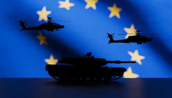 Large EU flag in the background with modern military equipment in front in silhouette