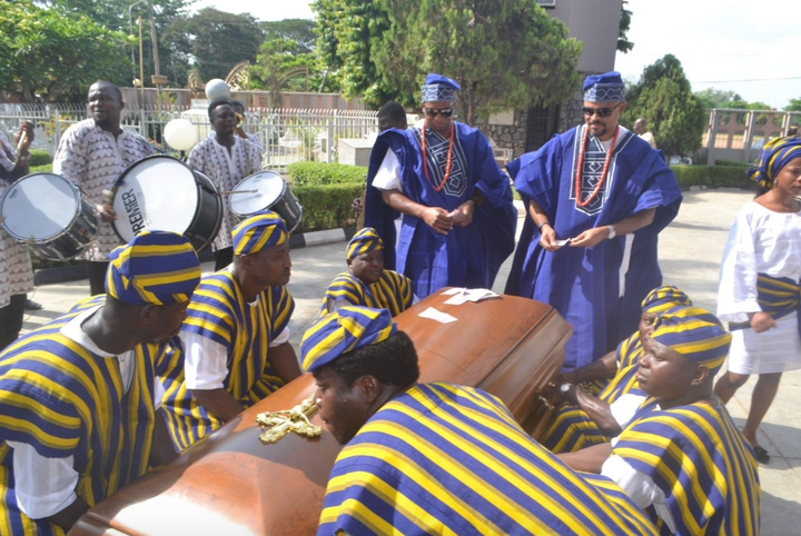 Just before the author's father's funeral, Mike, the author's husband (left), and Femi, the author's brother, put money on the coffin, a sign of respect.