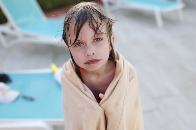 Little frozen girl in towel standing near swimming pool. Hypothermia in children concept