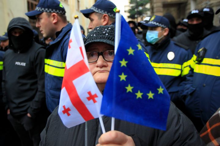 A woman with EU and Georgian national flags stands in front of police blocking a street during a rally to demand new parliamentary elections in the country, near the Parliament's building in Tbilisi, Georgia, on Nov. 25, 2024.