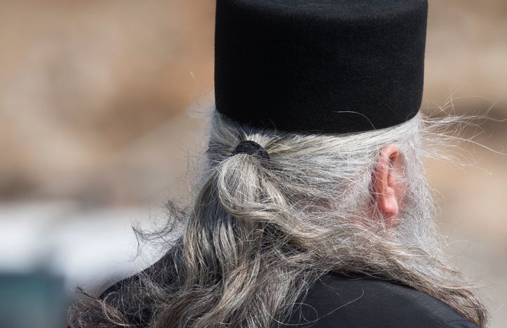 Greece 06/01/2019 Folegandros island church. Cyclades islands, Aegean sea. Priest seen from behind with lovely long hair.