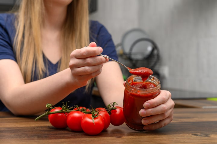 Tomato paste on a spoon next to fresh tomatoes