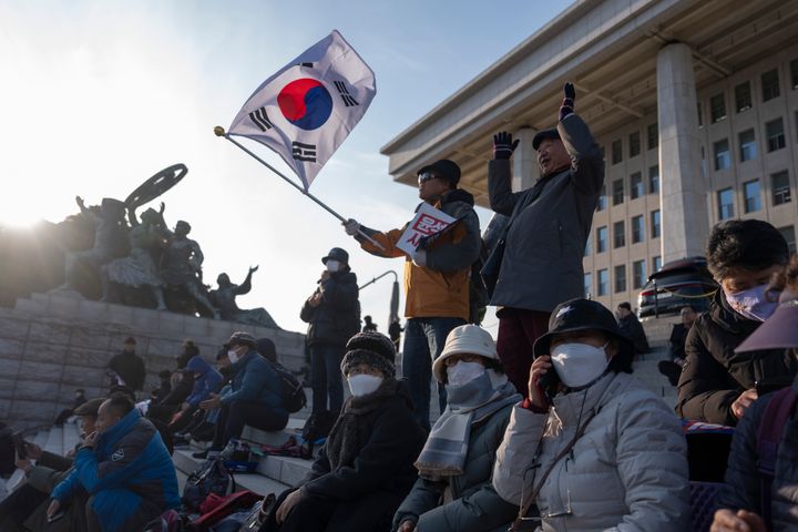 A protester waves a South Korean flag as he joins others gathering outside the National Assembly in Seoul, South Korea, Wednesday, Dec. 4, 2024.