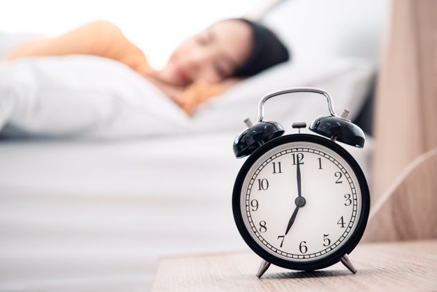 Young woman sleeping on bed with alarm clock in morning.