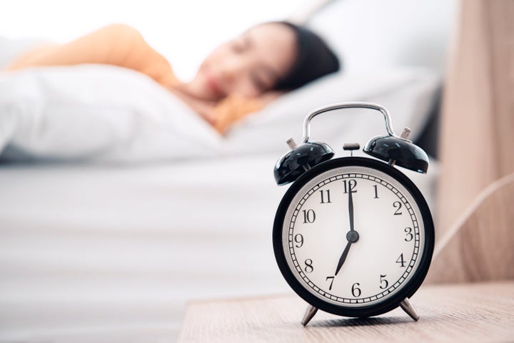 Young woman sleeping on bed with alarm clock in morning.