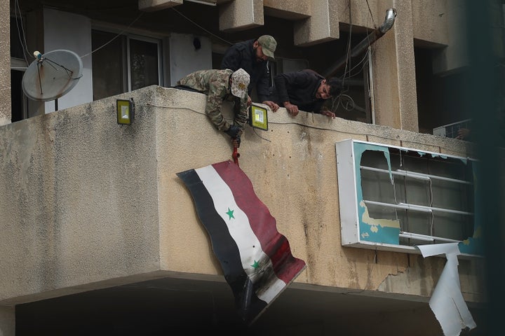 Syrian opposition fighters remove a government Syrian flag from an official building in Salamiyah, east of Hama, Syria Syria, Saturday Dec. 7, 2024. (AP Photo/Ghaith Alsayed)