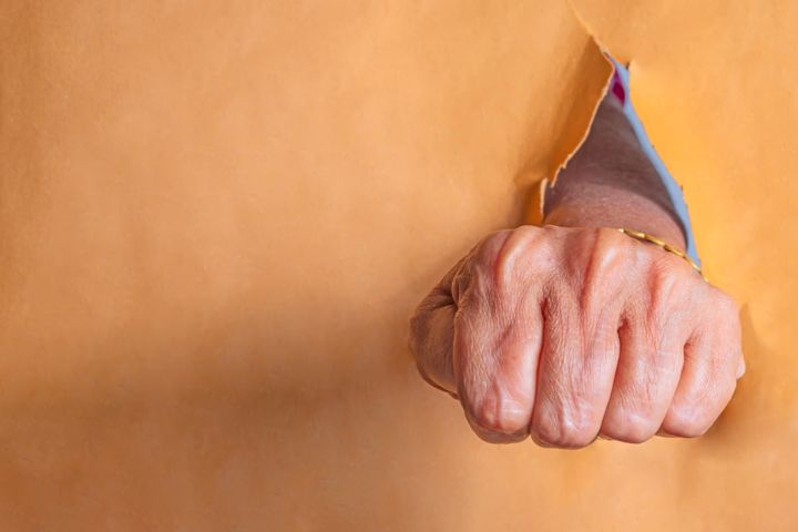 Hands of a senior woman punching through a hole in a paper. Close up