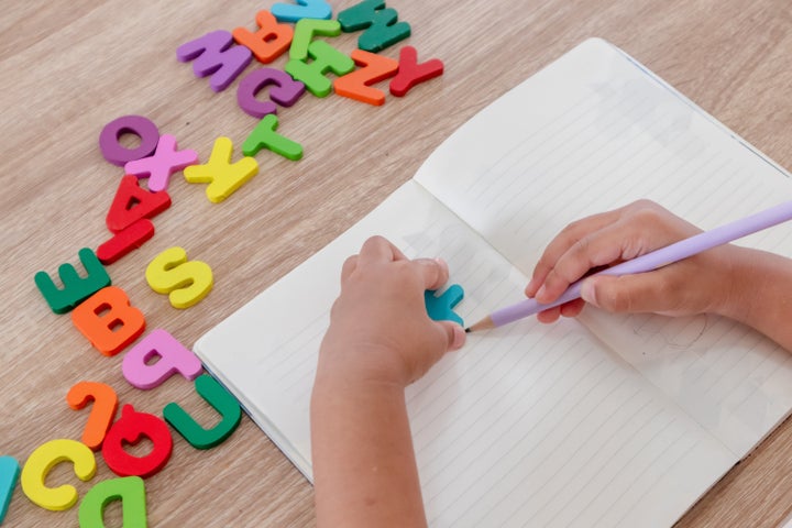 A little girl learning to write letters in a notebook with wooden alphabet letters on the table