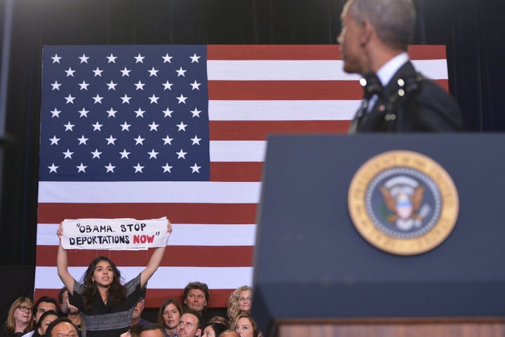 A protester holds up a banner as a guest beside her reaches to pull it away as then-President Barack Obama speaks on immigration reform at the Copernicus Community Center on Nov. 25, 2014, in Chicago.