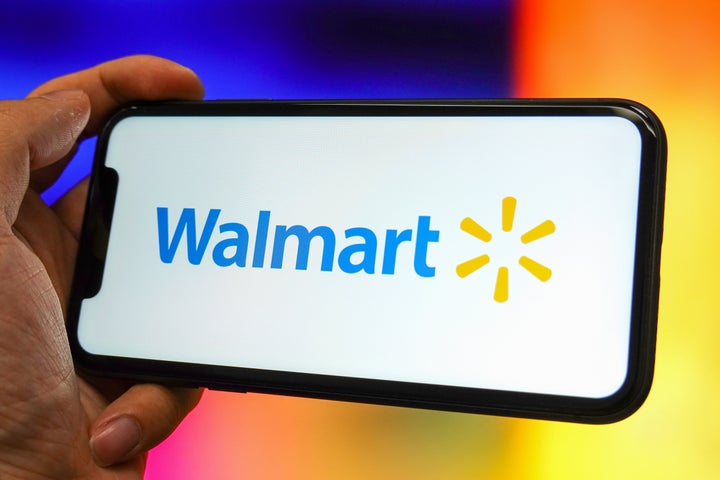 A Walmart logo is displayed on the screen of a smartphone. The CFPB has sued the company and financial services firm Branch Messenger for allegedly requiring delivery drivers to use an app that charged them fees to access their own earnings.