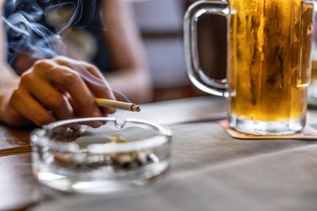 The hand of a smoking man or woman on a table led an ashtray with draft beer in a pub.