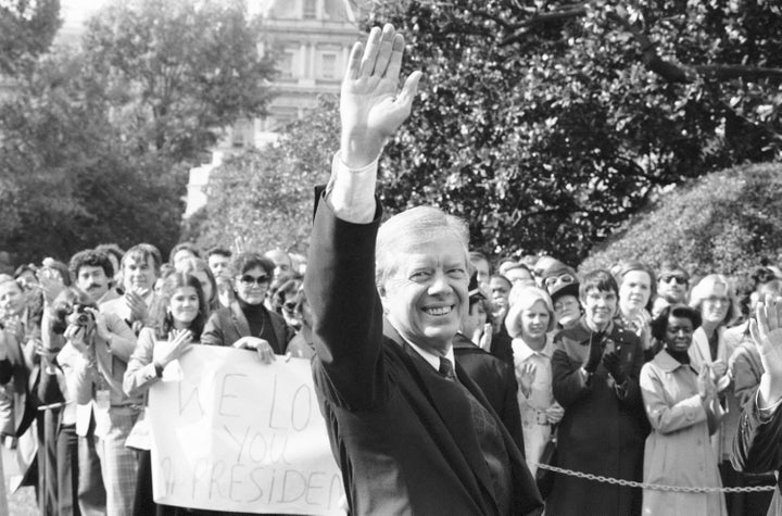 FILE - U.S. President Jimmy Carter waves as staff holds up sign proclaiming "We Love you Mr. President" in Washington, Nov. 5, 1980, as the president walks to helicopter for trip to Camp David, Md. (AP Photo, File)