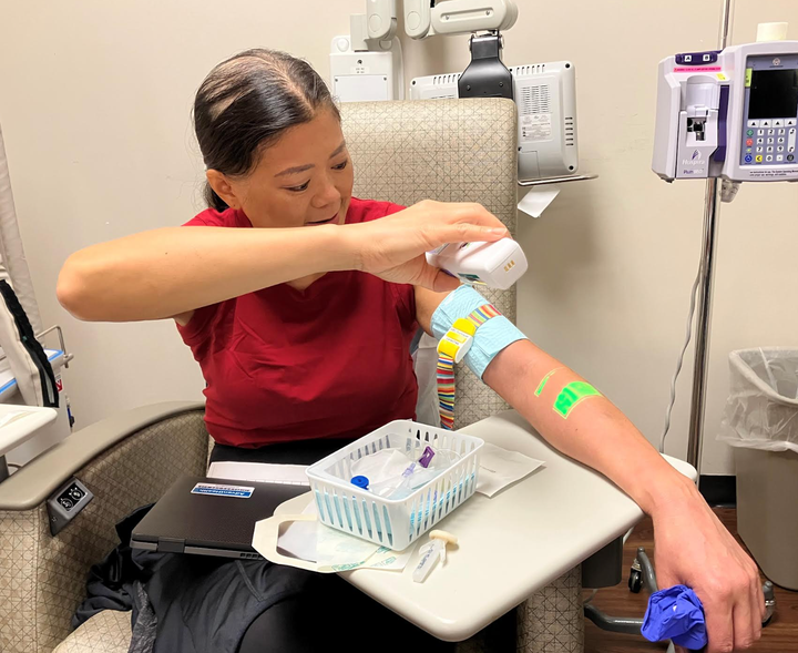 The author using a vein finder to help the nurses locate a vein so chemotherapy can be delivered.
