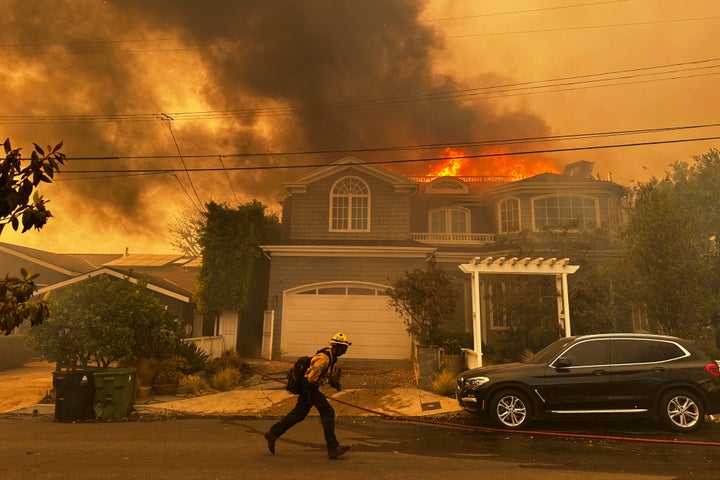 A residence burns as a firefighter battles the Palisades Fire.