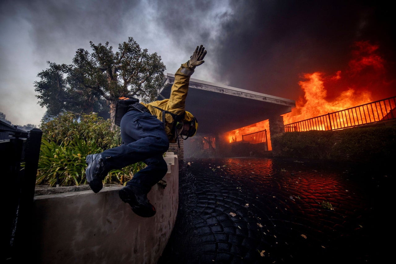 A firefighter jumps over a fence while fighting the Palisades Fire.