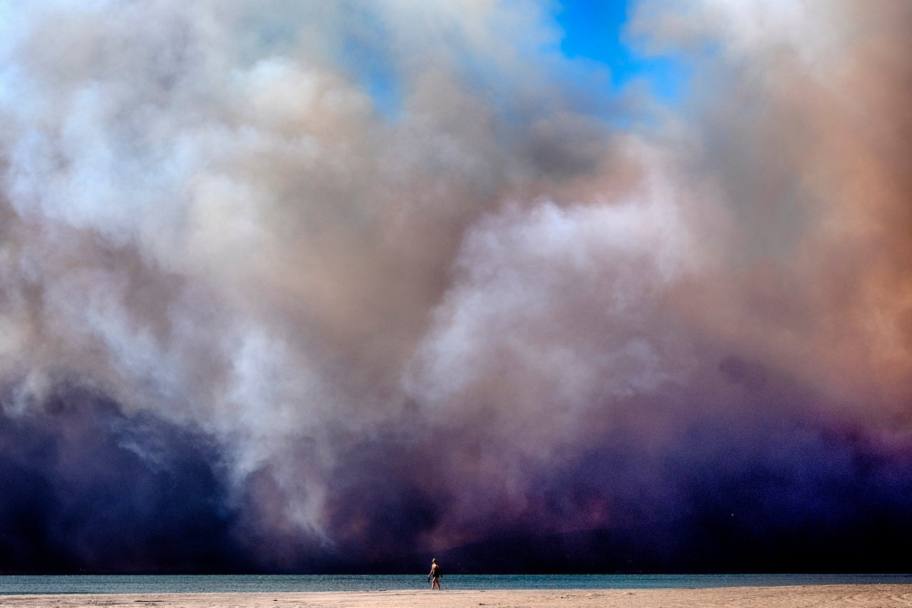 A lone beachgoer walks along the coast as a large, dark plume of smoke passes over the beach from a Pacific Palisades wildfire in Santa Monica on Tuesday.