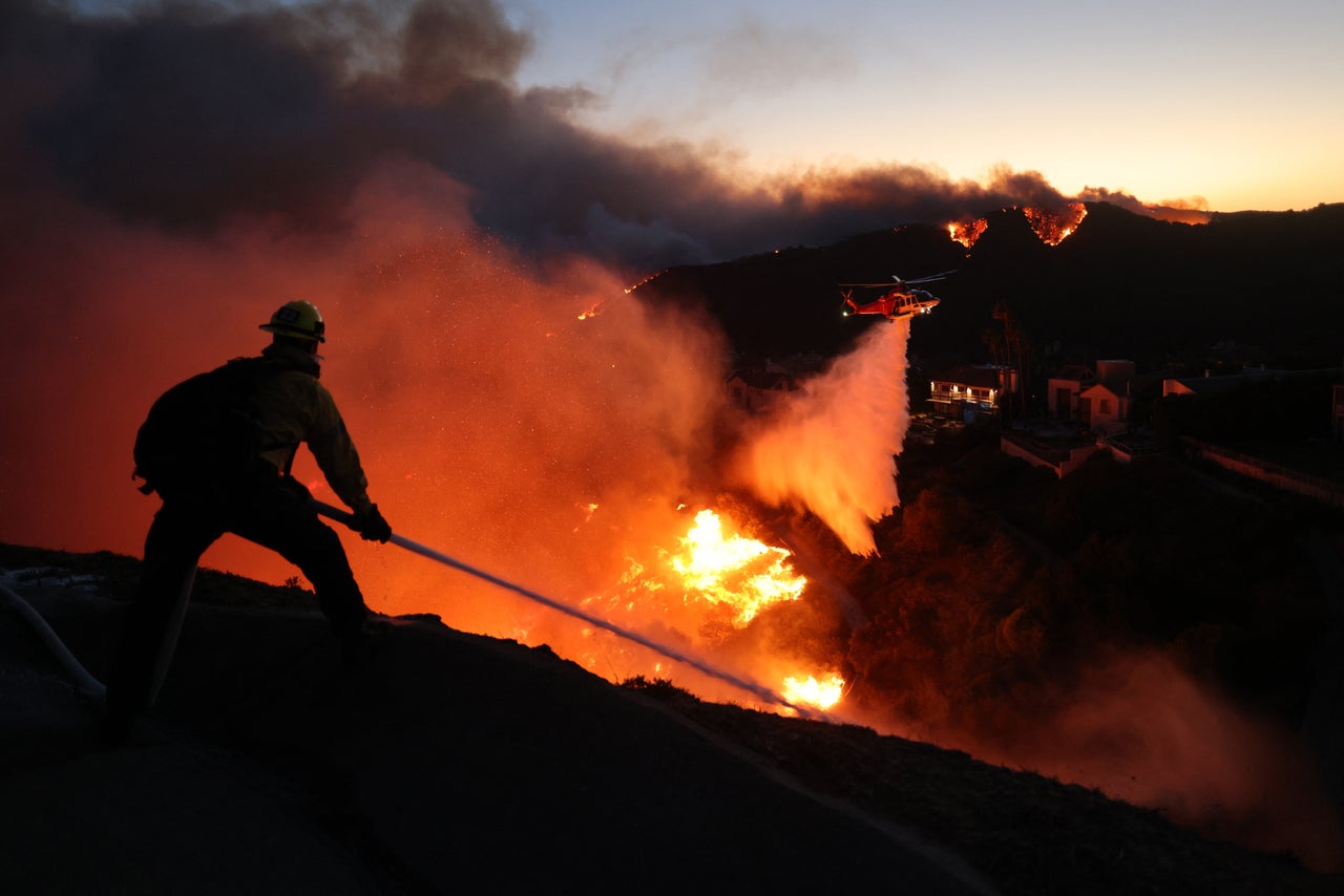 A firefighter douses flames as a helicopter drops water around homes threatened by the wind-driven Palisades Fire on Tuesday.