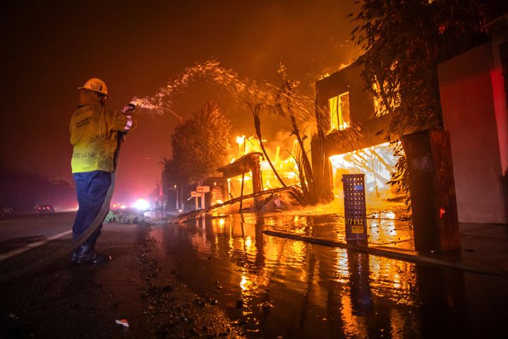 A firefighter battles the Palisades fire as it burns homes at Pacific Coast Highway amid a powerful windstorm on Jan. 8 in Los Angeles.