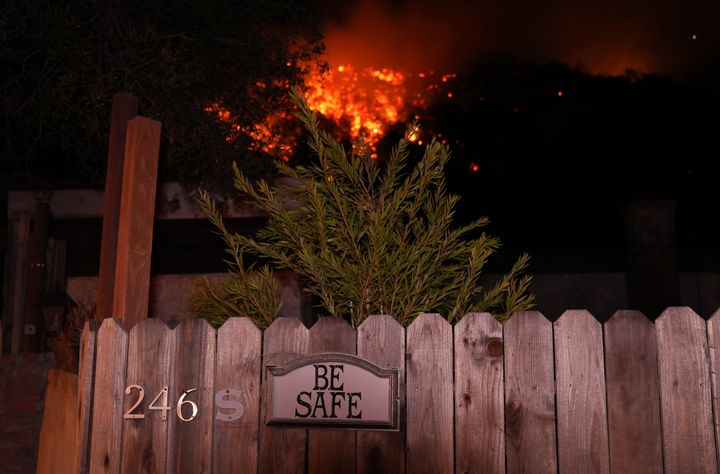 A 'Be Safe' sign hangs on a fence as wildfires rage in the background in Los Angeles on Friday.