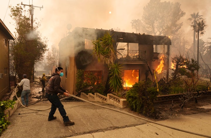 Pedestrians help a firefighter stretch a hose for a burning apartment building, on Wednesday, Jan. 8, 2025, in the Altadena section of Pasadena, Calif.