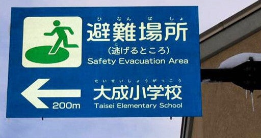 外国人にも伝わりやすいよう、やさしい日本語も併記した道路標識。「避難場所」を「逃げるところ」と言い換えている（青森県弘前市提供）